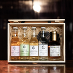 Öppen trälåda med fem flaskor från Infused Liquid på en bardisk med mörk bakgrund.