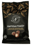 Svart påse från Narr Chocolate med guldfärgade kakaoblad och texten Havssaltsnöt, med bild på hasselnötter dragerade med mjölkchoklad, mot vit bakgrund.
