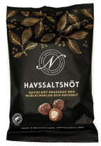 Svart påse från Narr Chocolate med guldfärgade kakaoblad och texten Havssaltsnöt, med bild på hasselnötter dragerade med mjölkchoklad, mot vit bakgrund.