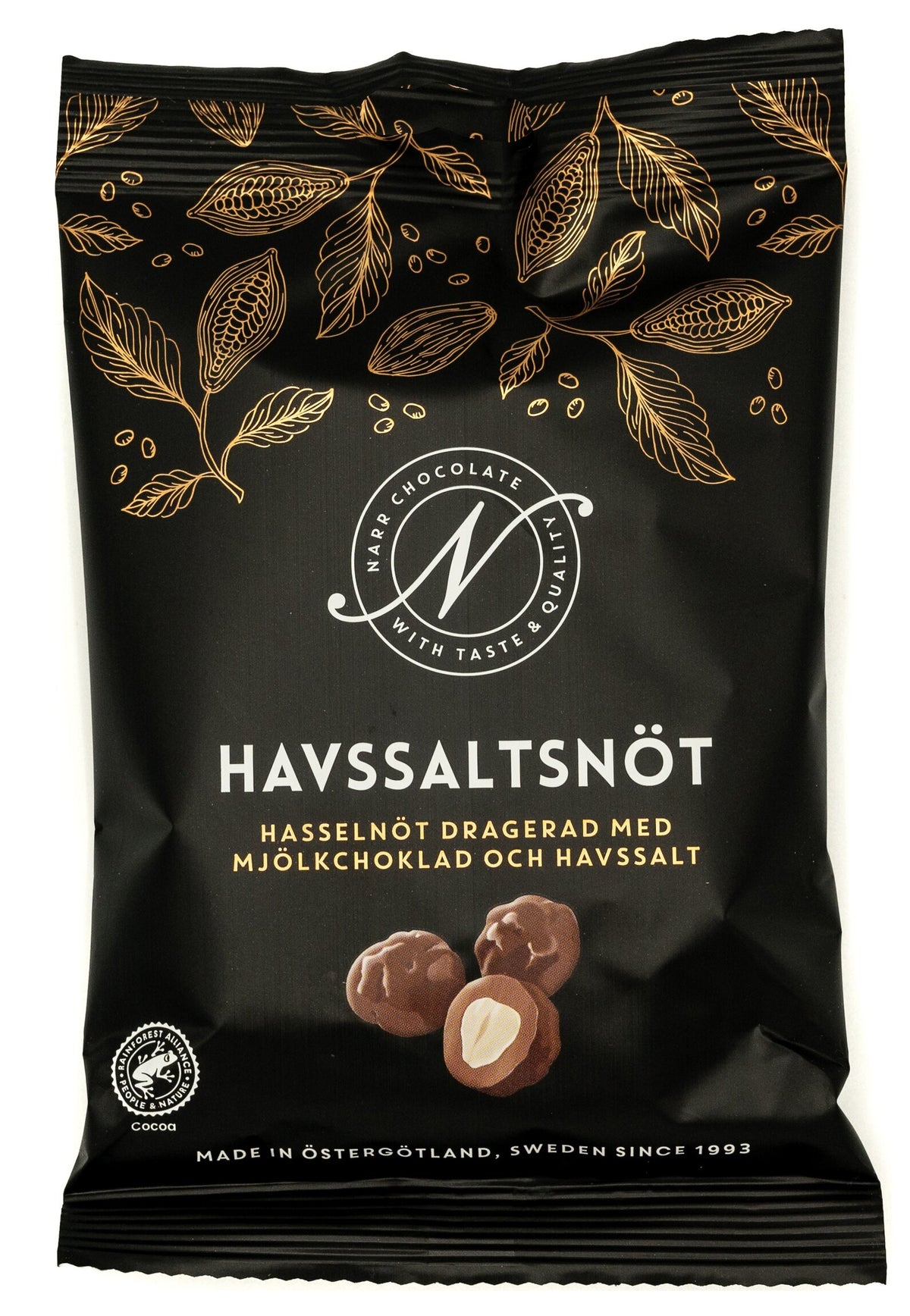 Svart påse från Narr Chocolate med guldfärgade kakaoblad och texten Havssaltsnöt, med bild på hasselnötter dragerade med mjölkchoklad, mot vit bakgrund.
